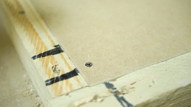 Screwing a screw into a drawer runner on side of wooden drawer using a battery drill. Furniture assembly. Master drills a hole drill. Master drills a hole in the board drill