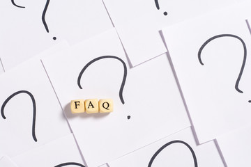 Faq acronym on wooden cubes against white note paper with handwritten question marks as background