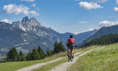 Fototapeta premium nice and active senior woman, riding her e-mountainbike in the Tannheim valley, Tirol, Austria with the village of Tannheim and famous summits Gimpel and Rote Flueh