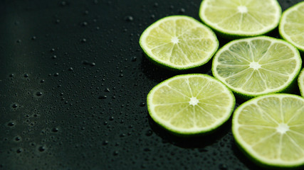 From above slices of fresh green sour lime on dark table with water drops 