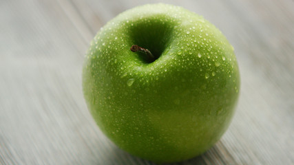 Closeup shot of green wet apple placed on light wooden background 