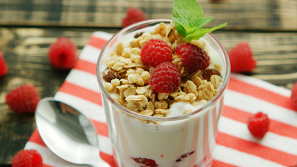 Closeup shot of glass with white yogurt and red raspberries with granola on top served on napkin