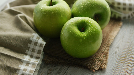 From above closeup shot of composed fresh green apples in water drops composed on napkin on wooden table
