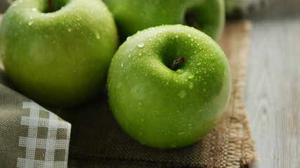 Closeup shot of whole ripe green apples with shiny drops of water composed on canvas napkin in daylight