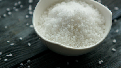 From above white salt in a bowl placed on dark wooden table
