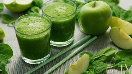 Layout of few glasses filled with green smoothie and served on table with green apples and spinach leaves