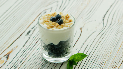 Served snack in glass with layered blueberries and yogurt topped with granola on wooden table
