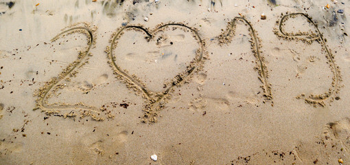 2019 written on the sea sand with heart shaped number 0. Natural sand textured background. New year and travel plans  coming soon concept, panoramic image 