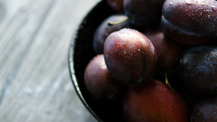 Closeup shot of bowl full of freshly washed wet plums of dark purple colors reflecting soft daylight