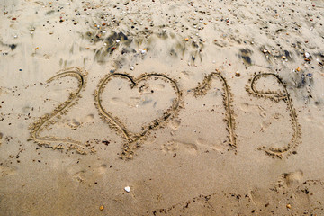 2019 written on the sea sand with heart shaped number 0.   Natural sand textured background. New year and travel plans  coming soon concept