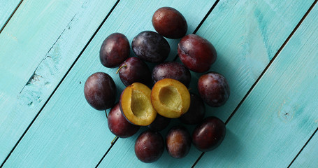 From above shot of composed pile of fresh plums with few halves on top of blue wooden table