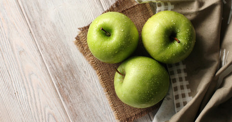 From above shot of wet ripe green apples in shiny water drops compose on napkin on wooden table in daylight