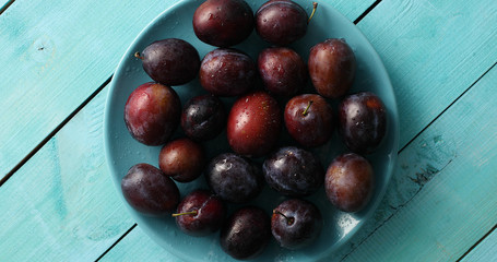 Top view of pile of fresh ripe plums on blue plate composed on wooden blue table