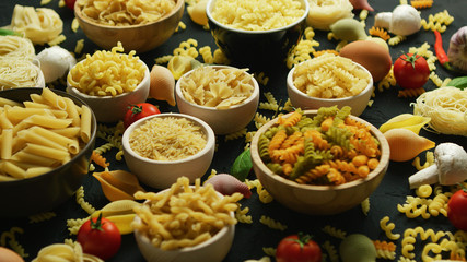From above view of white bowls full of macaroni of different shape and color on black background