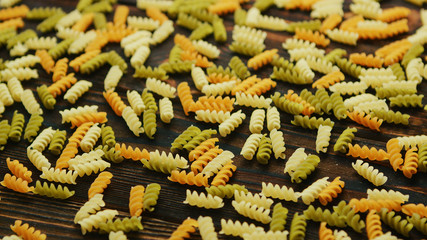 From above view of colorful uncooked fusilli pasta laid in disorder on wooden background 