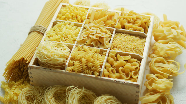 Wooden box filled with plenty of various macaroni and pasta with spaghetti in bunch