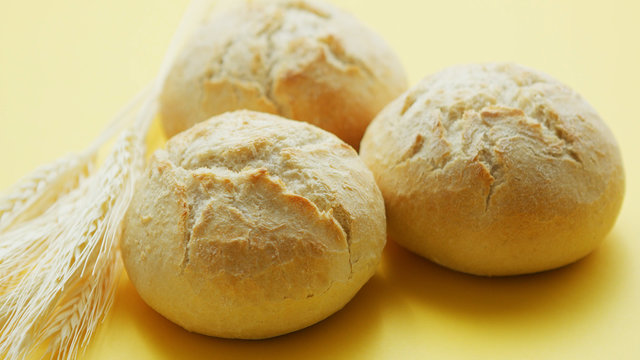 From above view of three round loafs of bread with wheat placed near on yellow background