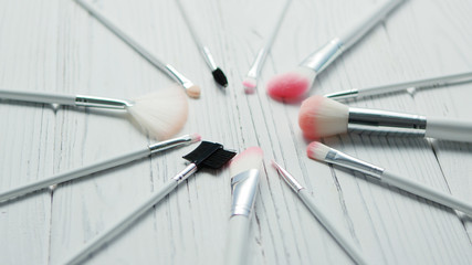 From above view of different brushes for makeup laid in circle on white wooden background 