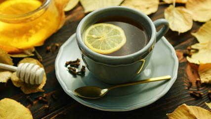 From above view of cup of hot tea with slice of lemon and bowl of honey placed near decorated with dry leaves on wooden background