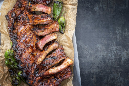 Barbecue spare ribs St Louis cut with hot honey chili marinade and jalapeno as top view in a rustic skillet and backing paper with copy space right