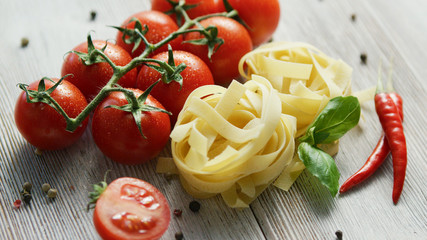 Raw small heaps of uncooked pasta on table with fresh tomatoes and chili pepper with basil leaves 