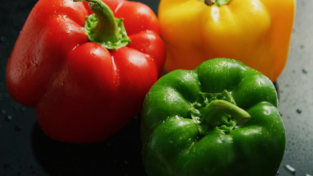 Closeup of shiny bell peppers of different colors with wet surface in water drops