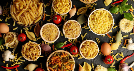 From above shot of arranged bowls with uncooked macaroni and pasta on table with various ingredients for cooking