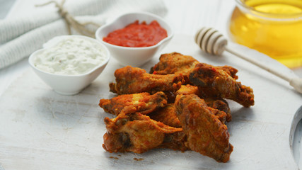 Closeup of golden crispy fried chicken wings served on board with different sauces 