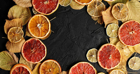 From above shot of arranged wreath on black surface with dry leaves and dry citrus slices