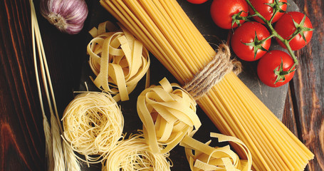 Top view of uncooked mix of pasta and spaghetti on board with grapevine tomatoes and garlic bulb