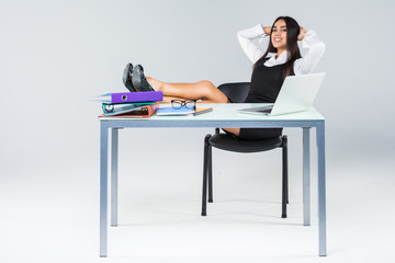 Young relaxed business woman with legs on working table enjoy the end of working day isolated on gray background