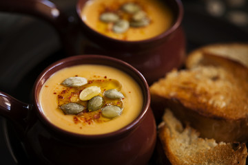 Autumn homemade cream soup of roasted pumpkin with croutons or toasted bread and seeds in a vintage ceramic bowls for Halloween or Thanksgiving day close-up on dark background.Healthy vegan food