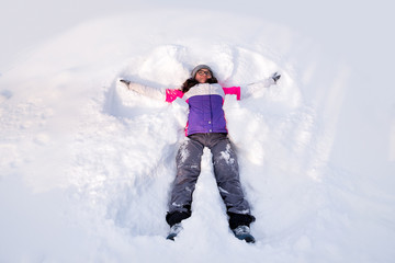 Fototapeta na wymiar girl in the snow makes an imprint in the shape of a snow angel