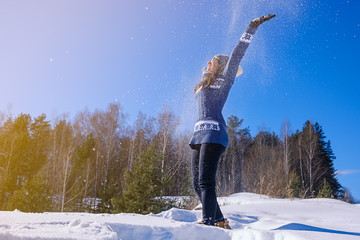 girl in a warm sweater throws snow and bask in the winter sun