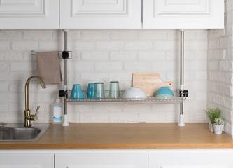 Clean dishes drying on metal dish rack on light background. Kitchen utensils and dishware on wooden shelf. Kitchen interior background.Text space.