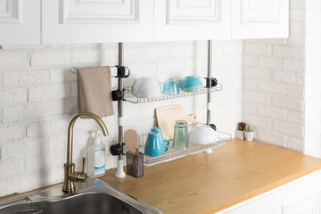 Clean dishes drying on metal dish rack on light background. Kitchen utensils and dishware on wooden shelf. Kitchen interior background.Text space.