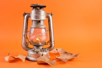 Old retro gas lantern with burning light and fallen dry leaves isolated on orange background. Autumn concept. Close up, selective focus © Emilija
