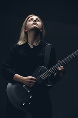 Blonde guitar girl on dark scene, black wall