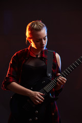 Fototapeta premium Blonde woman play guitar on stage, red, blue light dark scene