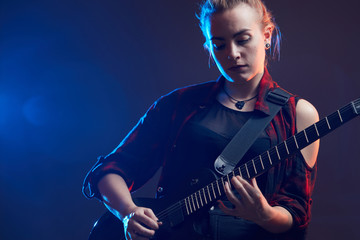 Obraz premium Blonde woman play guitar on stage, red, blue light dark scene