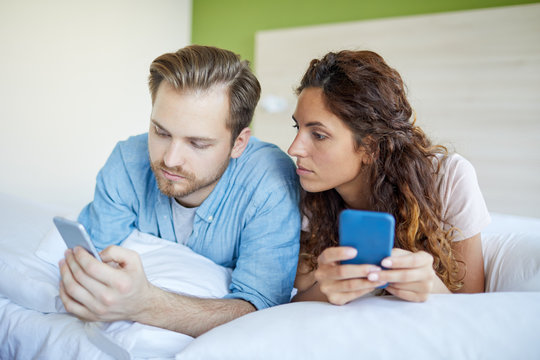 Young couple lying on bed and searching or texting in their smartphones