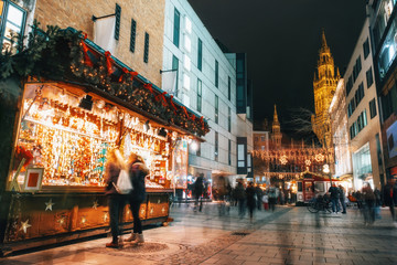 Obraz premium Blurred moved people and sales booth at the christmas market on Marienplatz against Town Hall Neues Rathaus in Munich, Germany