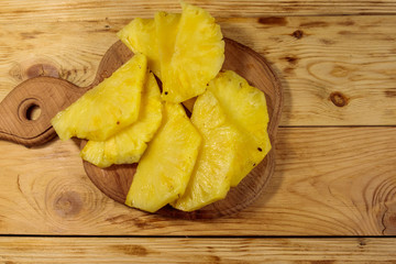 Pieces of pineapple on a cutting board on wooden table. Top view