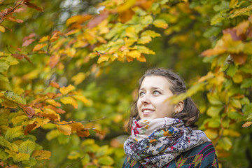 Close up Portrait of beautiful young smile woman in fall beech forest with yellow leaves around. Detail view on girl beauty with empty space in easy colorful background of tree crown.
