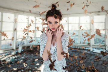 Red hair girl with freckles standing in the falling autumn leaves. Autumn concept