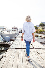 young cute blonde girl on a sunny afternoon walking along the promenade next to yachts