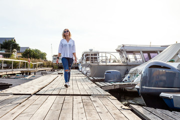 Fototapeta premium young cute blonde girl on a sunny afternoon walking along the promenade next to yachts