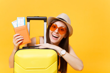 Fun tourist woman in summer casual clothes, hat, orange sunglasses with suitcase, passport isolated on yellow background. Passenger traveling abroad to travel on weekends getaway. Air flight concept.