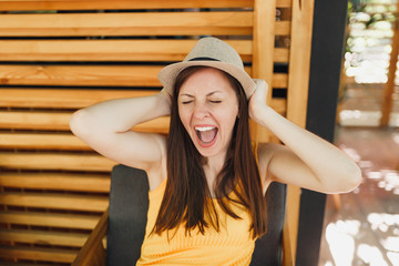 Portrait of excited smiling young woman in straw summer hat, yellow shirt put hands on head on wooden background in outdoors street summer coffee shop cafe. People sincere emotions, lifestyle concept.