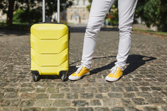 Cropped image of traveler tourist woman legs in yellow summer casual clothes with suitcase on road in city outdoor. Girl traveling abroad to travel on weekends getaway. Tourism journey lifestyle.